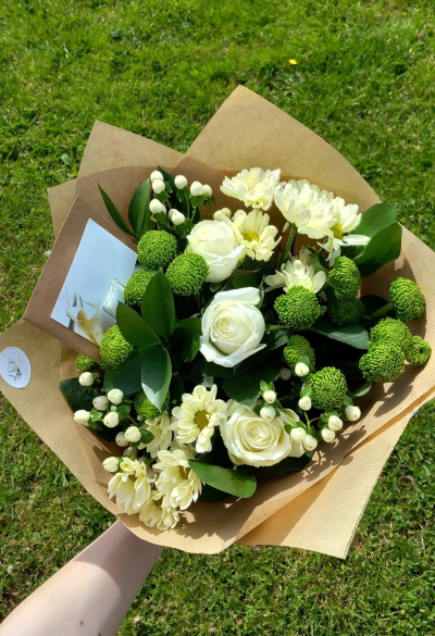 Ivory Charm - A naturally elegant hand-tied bouquet featuring crisp ivory tones, vibrant green textures, and fresh seasonal foliage, beautifully wrapped in rustic kraft paper. This charming arrangement brings a clean, modern feel and is perfect for thoughtful gifting, celebrations, or sending a touch of natural beauty to someone special.